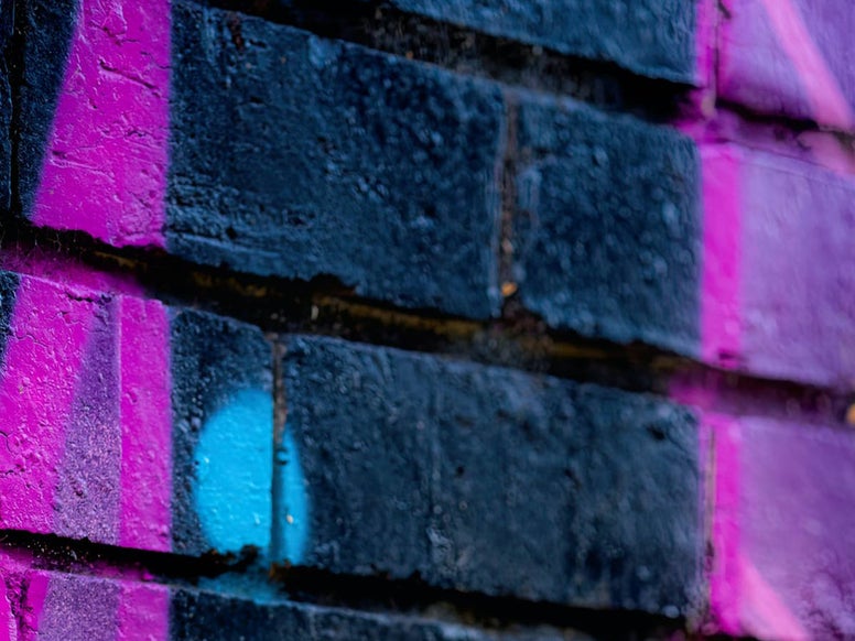 Bright pink grafitti on a black brick wall - Photo by Sneep Crew